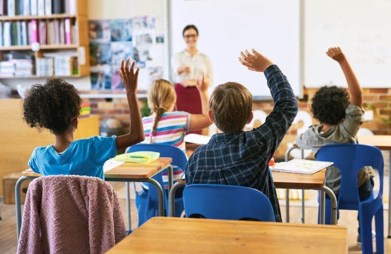 A classroom scene with children eagerly raising their hands to participate in the lesson.