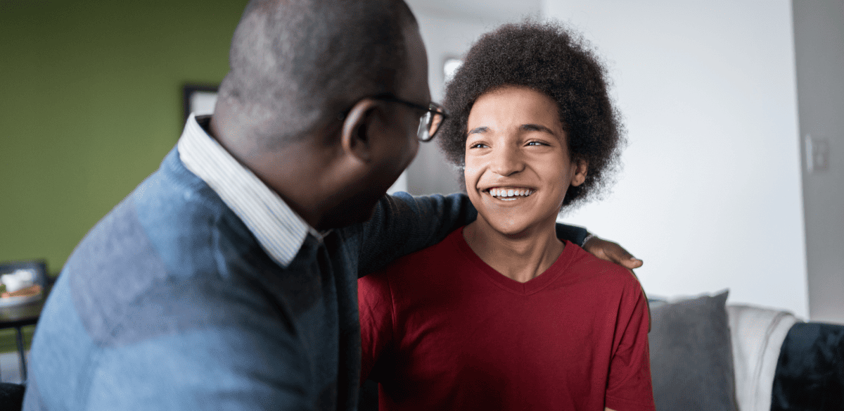 A man and a young boy share a joyful moment, both smiling brightly at the camera, showcasing their bond and happiness.