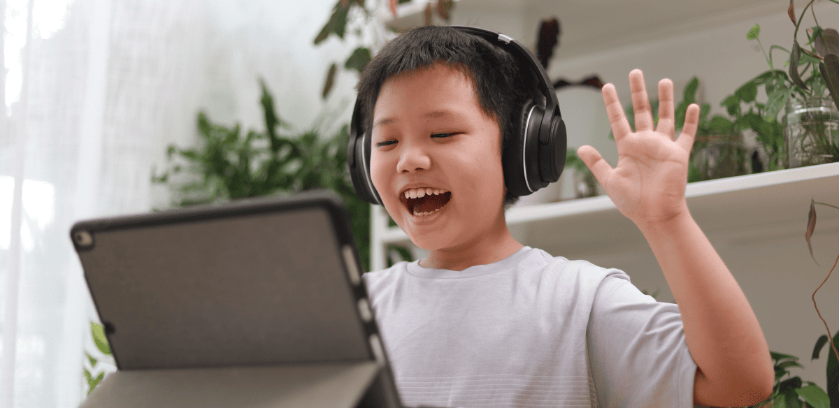 A young boy with headphones smiles while engaged with his laptop, showcasing joy in his digital experience.