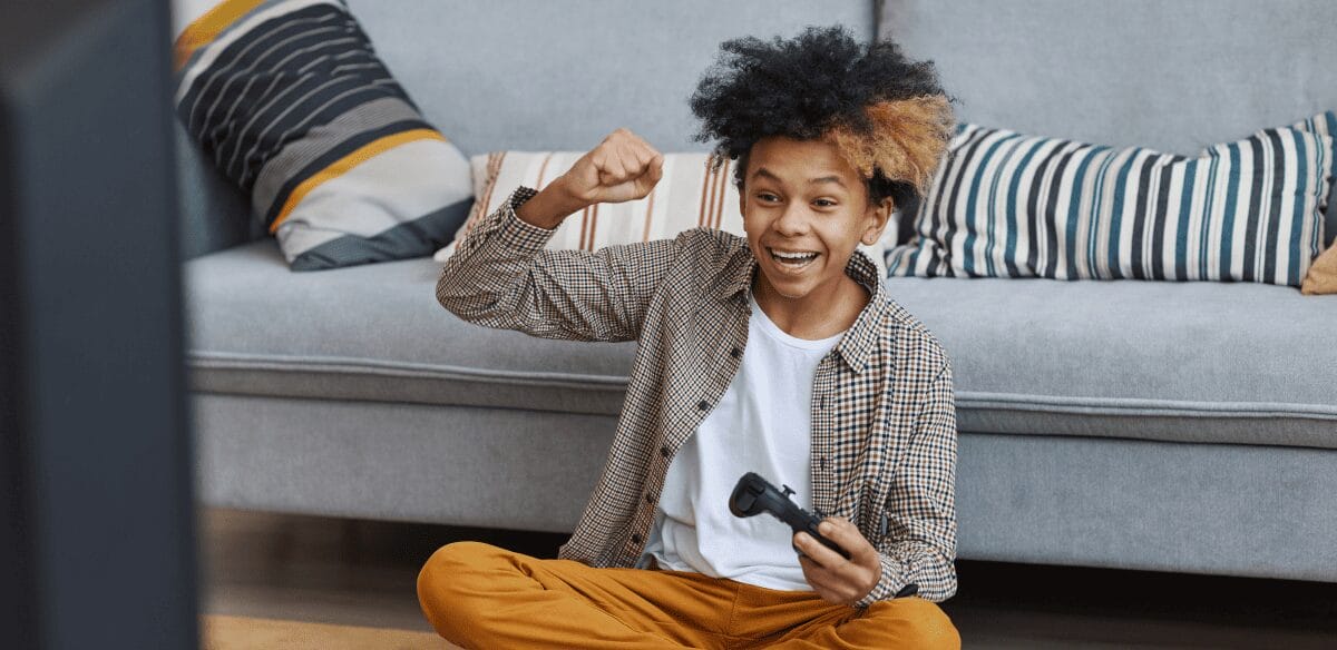 A young boy sits on the floor, focused on a remote control in his hands, surrounded by a playful atmosphere.