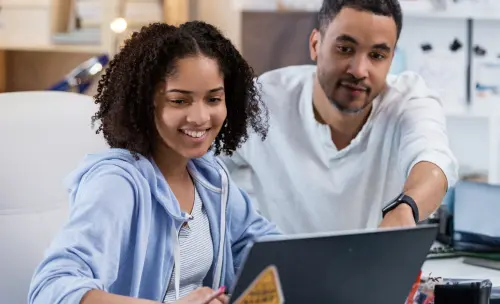 A man and woman smile at each other while viewing a laptop screen together, showcasing a moment of shared joy.