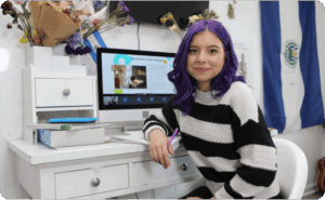 A woman with purple hair is seated at a desk, focused on her computer screen, creating a vibrant workspace.