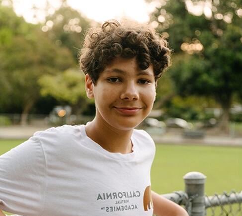 Student smiling at the camera wearing a white shirt with the California Virtual Academies logo in it